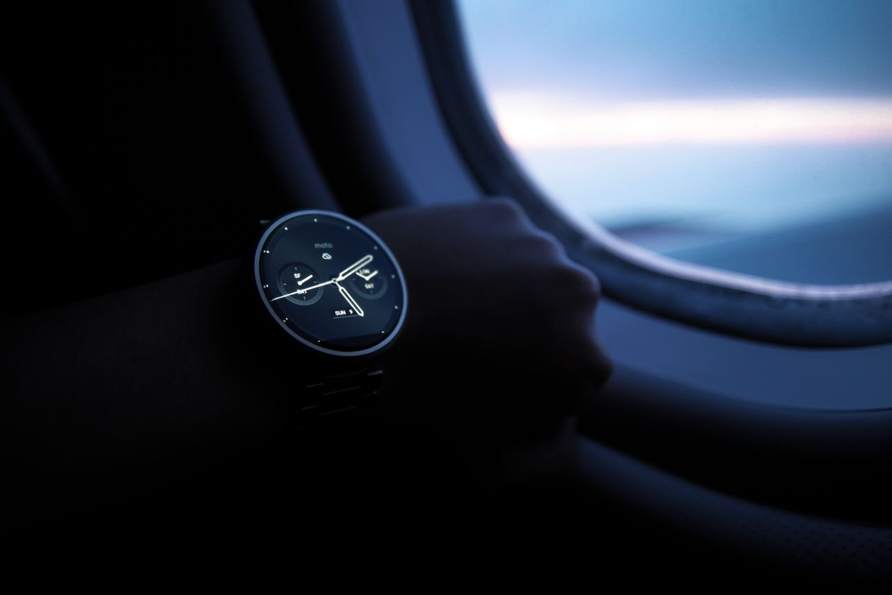 A smartwatch on a wrist shown against an airplane window view during flight.
